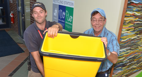 Rudy Sager and Al King from Facilities Management hoist one of the new yellow compost bins now located in the foyers of each building on campus.