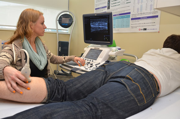 Carey Simpson conducts an ultrasound procedure on the calf of volunteer John Bocti.