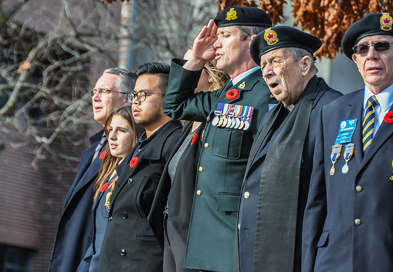 Lieutenant-Colonel Mike McGinty, centre, salutes while participants at UBC Okanagan's 2016 Remembrance Day service sing O'Canada.