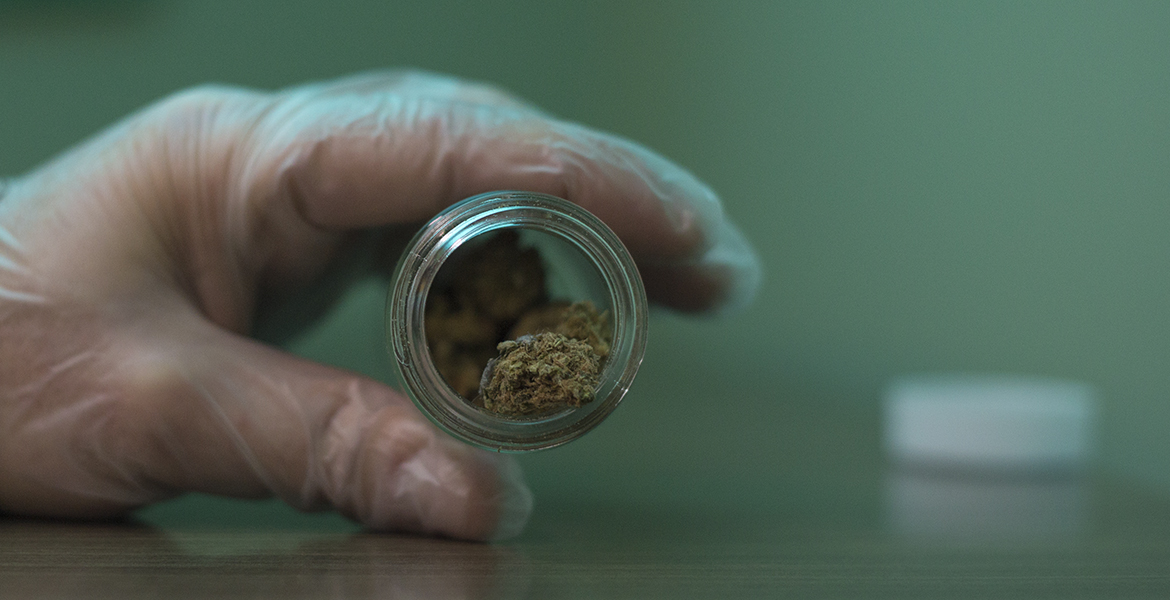Cannabis in a glass container being held by a gloved hand.