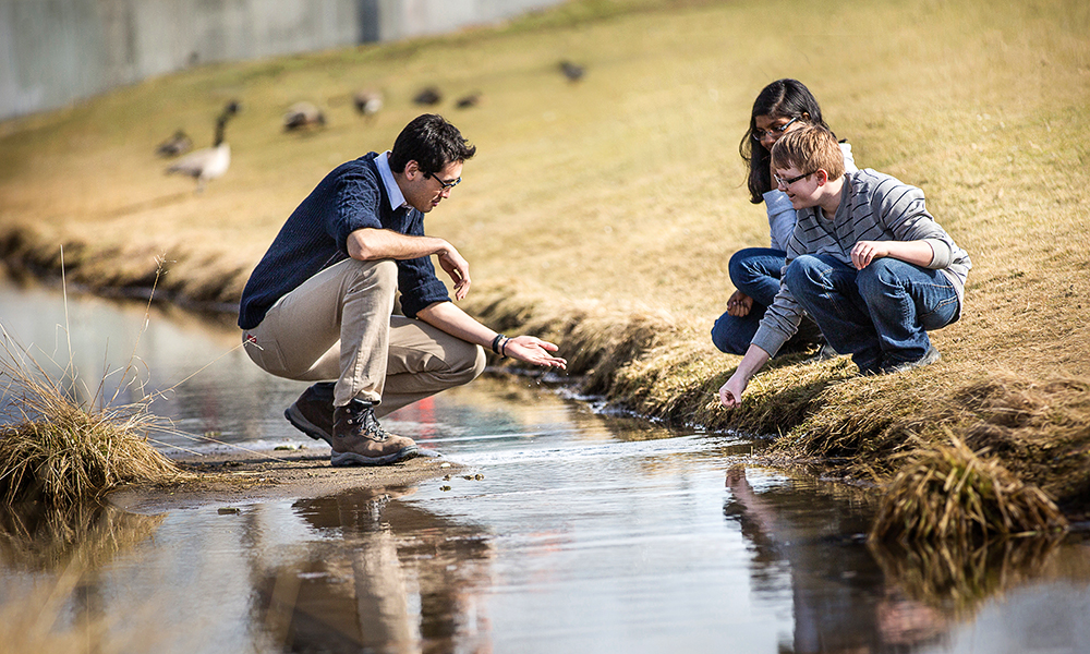 Students interacting with a teacher by a body of water
