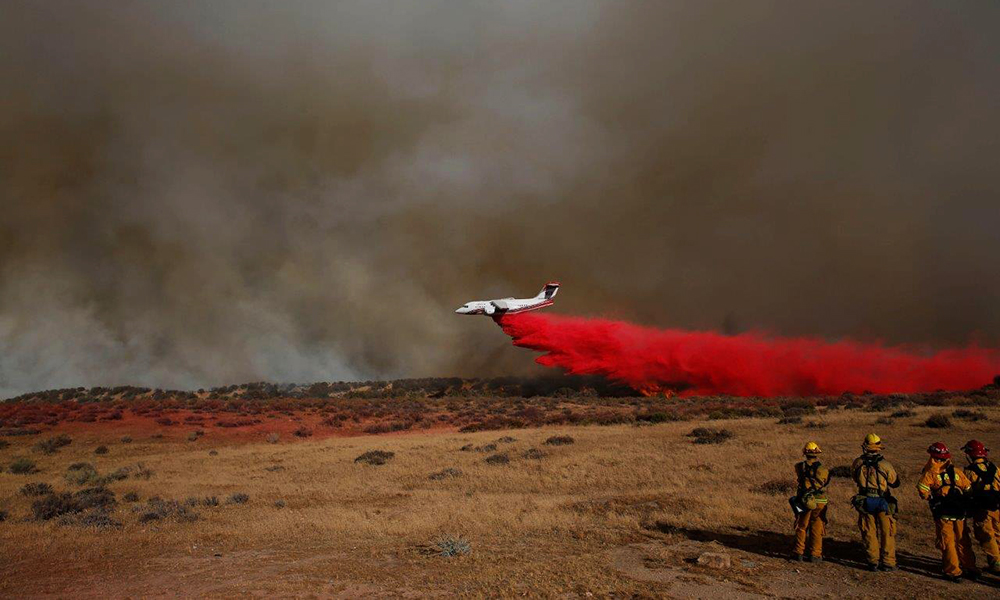 Aircraft dropping red fire retardant on a wildfire