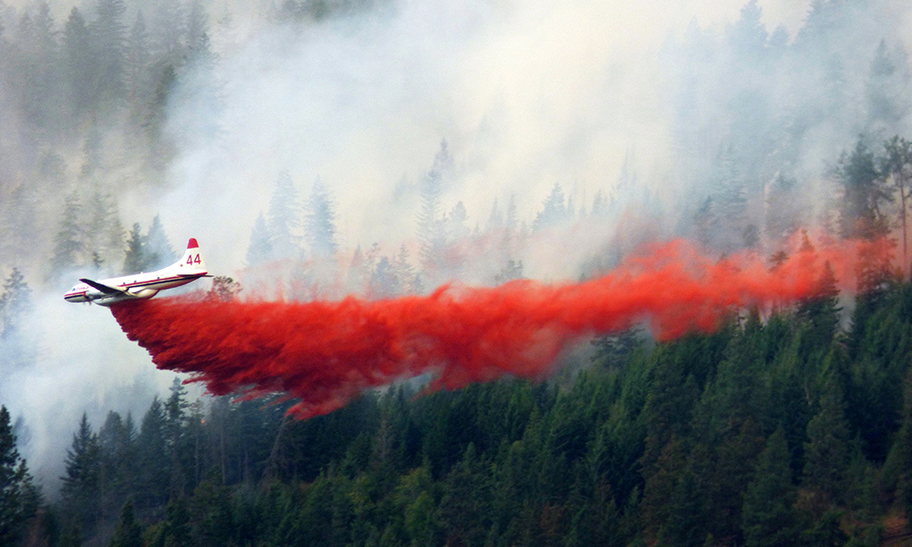 Aircraft dropping red fire retardant on a wildfire