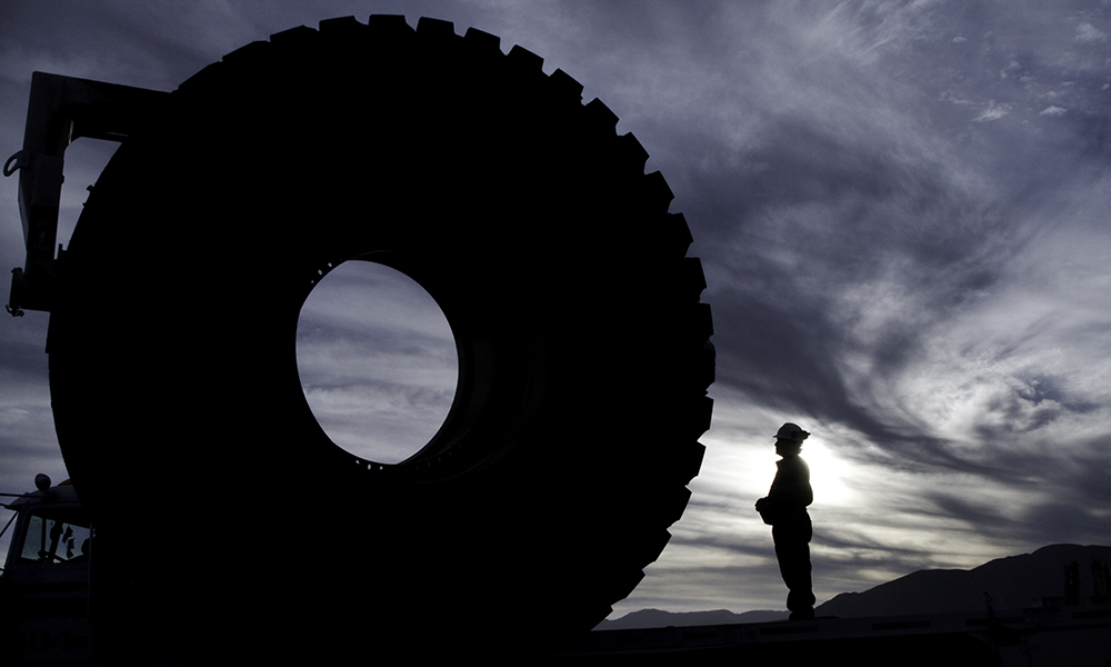Silhouette of a worker standing next to a massive tire.