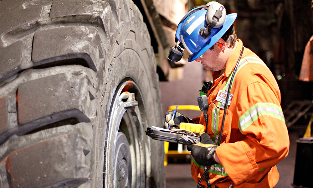 Man in coveralls and a hardhat inspecting a large tire.