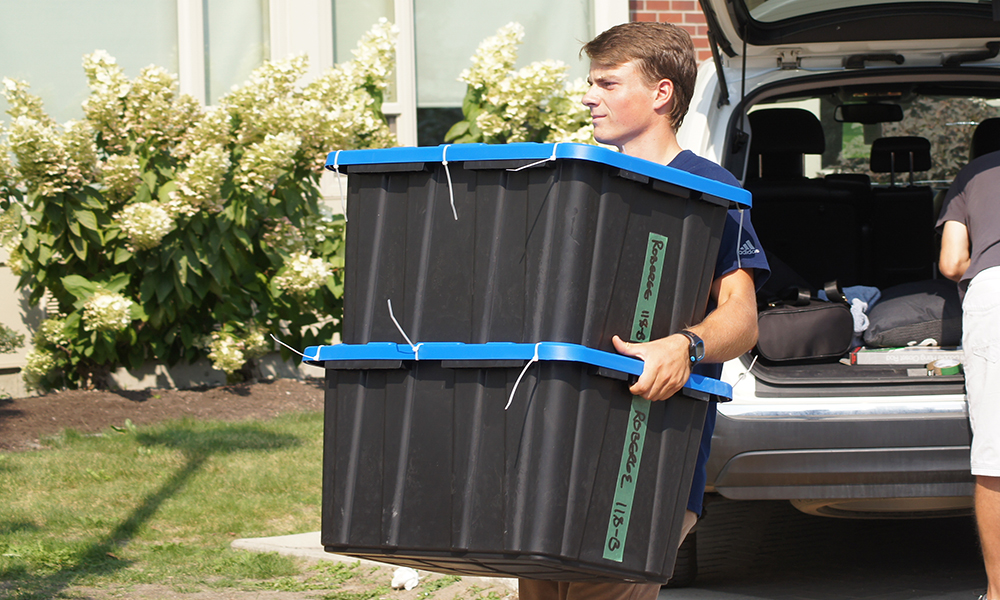 Man carrying two large black bins on Move In Day