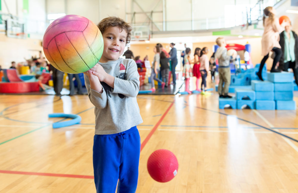 A child holding a ball in a gymnasium full of children