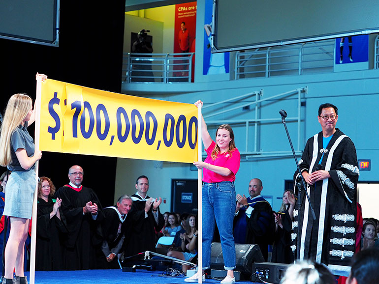 UBCO students Catherine Fleck-Vidal and Mykela White hold up a banner as President Santa Ono announces the $100,000,000 fundraising campaign has been met a year earlier than planned.