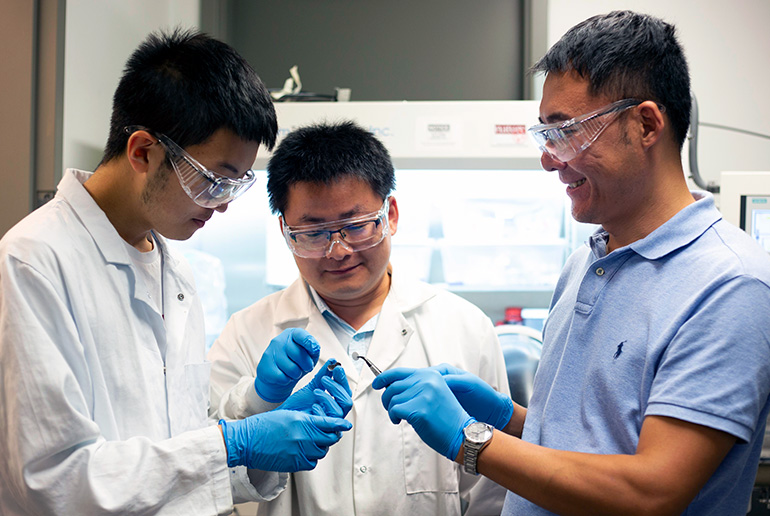 UBCO engineering students Peter Zhao and Huibing He examine the component of a tiny lithium-tellurium battery along with assistant professor Jian Liu (right).