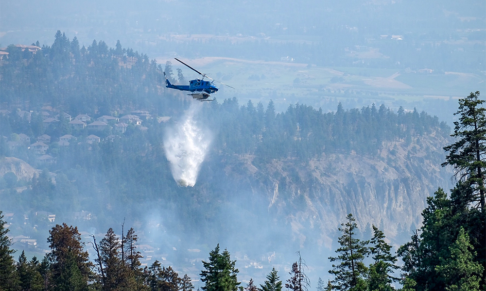 A helicopter dumping water on a forest wildfire