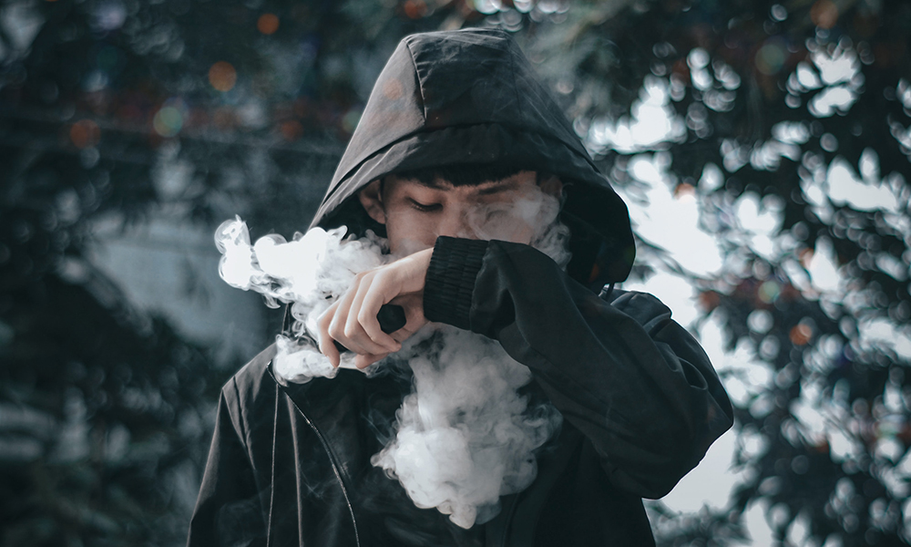 youth in a black hoodie is vaping