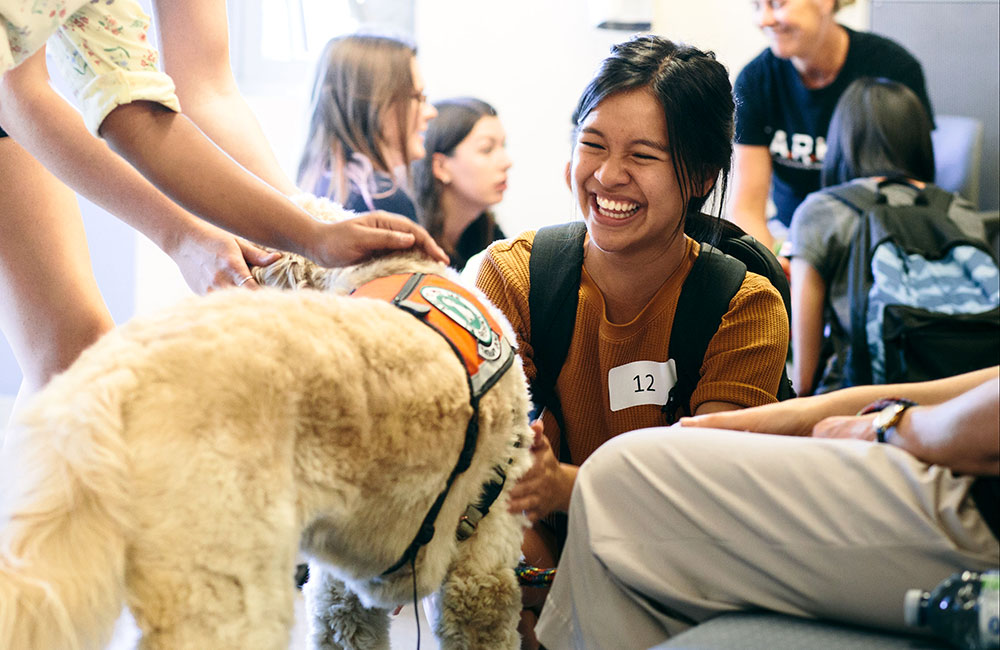 A student smiles with Cosmo, a labradoodle