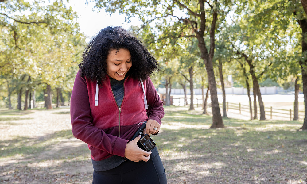 A young woman checks insulin pump and blood sugar monitor while hiking outdoors. 
