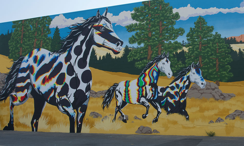 A colourful mural of three horses running across a brown and green landscape. The horses are painted in unique colours and shapes, helping them stand out against the brown landscape.