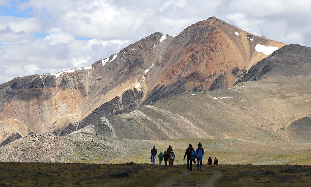 A landscape photo of four people walking against the shadow a giant mountain range