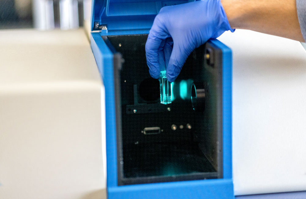 A cuvette containing a water sample is placed in a machine and glows teal