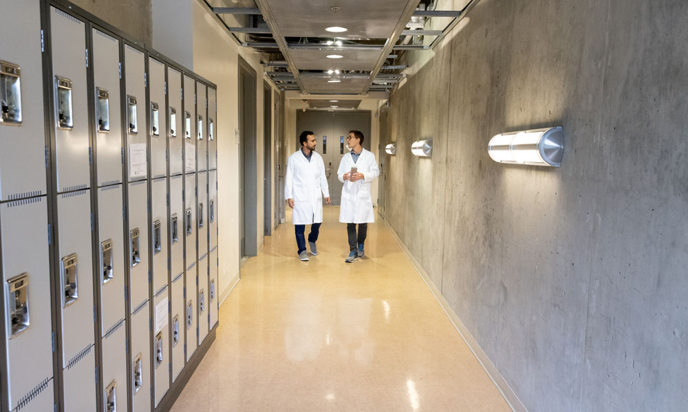 Dr. Anas Chaaban and Dr. Nicolas Peleato walk down a hallway flanked by lockers, speaking with one another