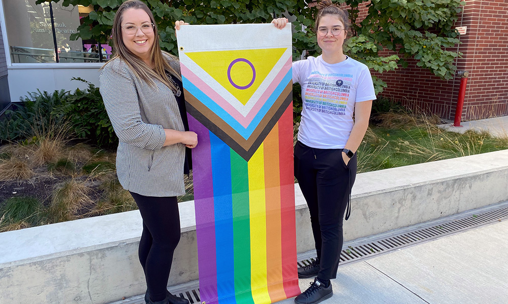Two students hold up Pride progress banners