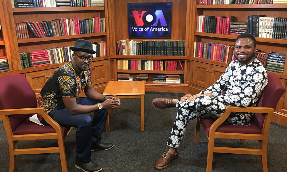 Segun David Fatudimu sitting on a set with the host of Voice of America, a radio program