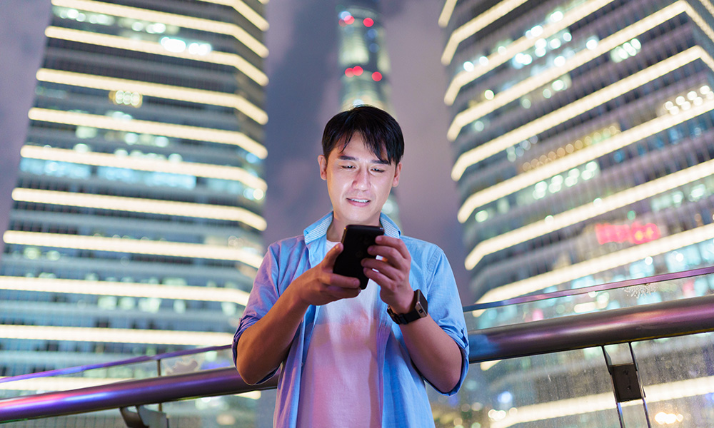 A photo of a young man using a smartphone at night.