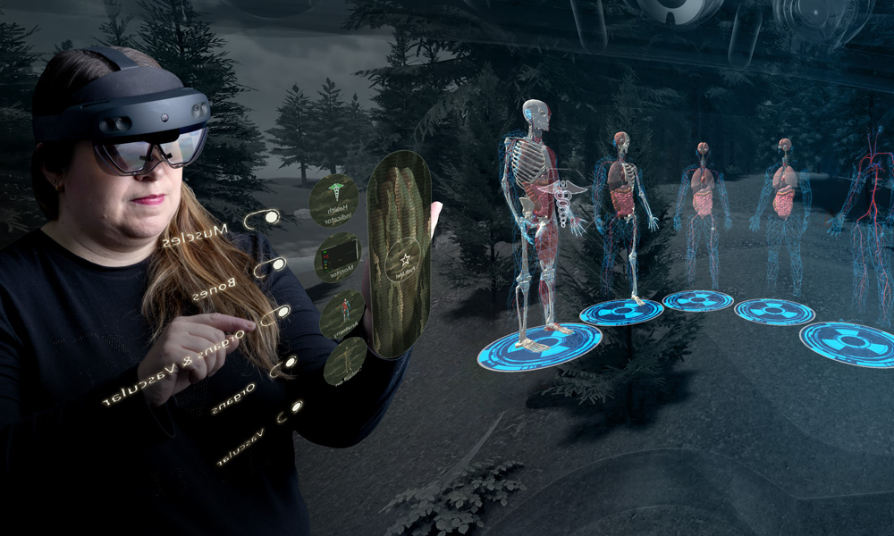 Carla Mather is pictured against a black background wearing a microsoft hololens. as she motions her hands in the air, a hologram is on her left, showing the viewer what she sees through the hololens. the hologram features skeletons with varying levels of vasculature
