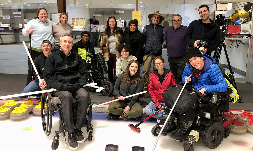 Heather Gainforth with a group of individuals at a curling rink, some of whom have a spinal cord injury