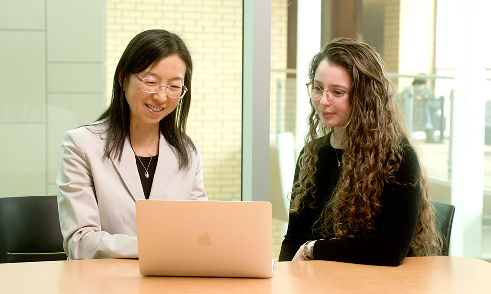 Dr. Claire Yan is pictured in front of a laptop with a student sitting next to her