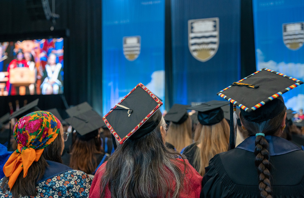 A photo of three students with their backs to the camera, focusing on their graduation hats which are beaded in multiple colours around the edges
