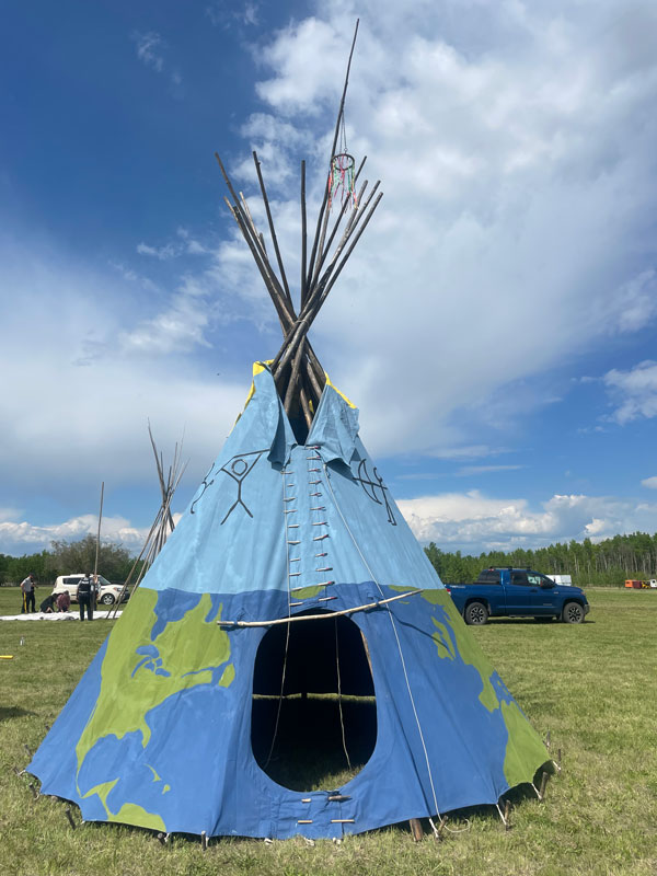 An assembled teepee with blue fabric covering the main body, and support poles pointing out the top.