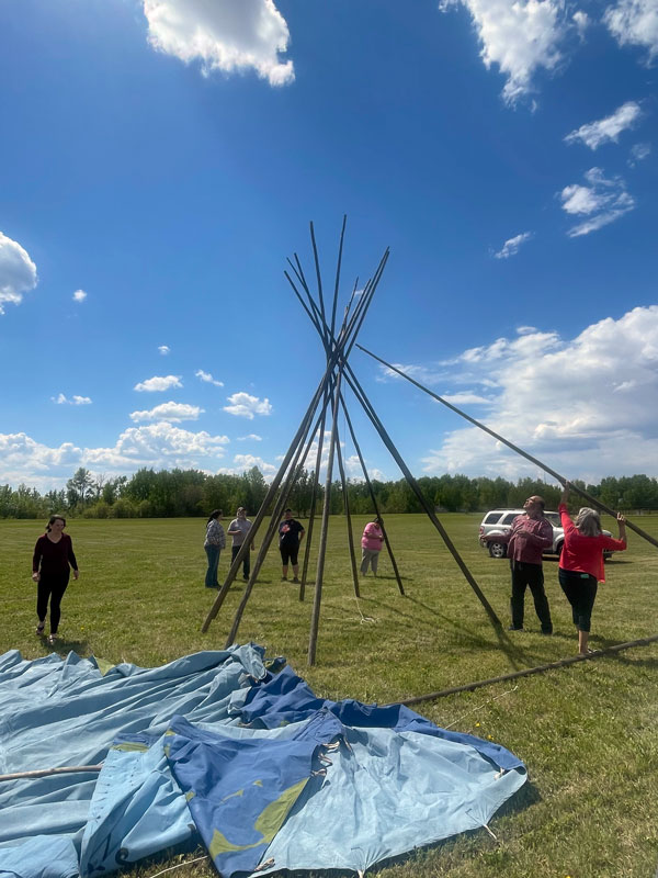 A group of people lean poles against each other to form the frame of a teepee