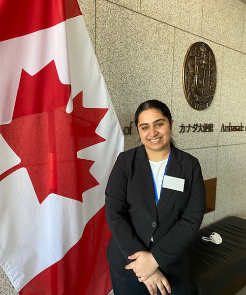 Puneet Kaur Aulakh standing in front of a Canadian flag, with japanese characters on the wall behind her.
