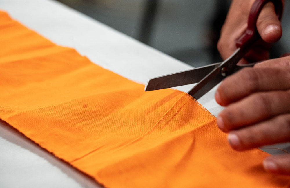 A close-up of fabric scissors cutting a piece of orange fabric to size