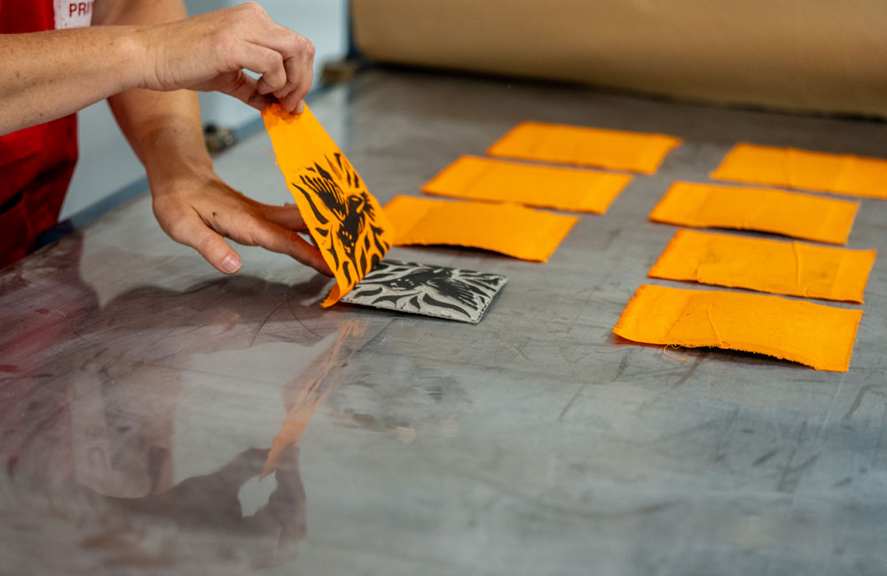 A close-up of a hand peeling apart the hummingbird lino and orange flag from each other