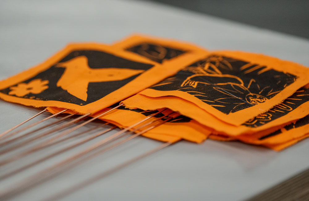 A close-up of a stack of completed orange flags, each printed with a unique drawing of a hummingbird