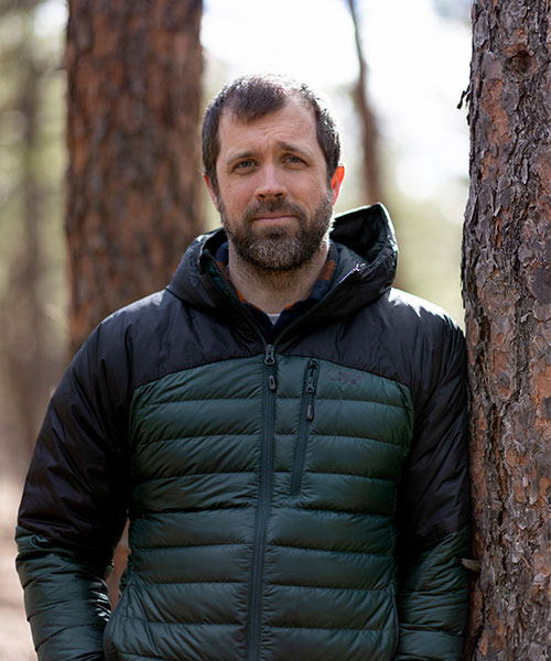A headshot of Dr. Mathieu Bourbonnais in the forest, leaning against a tree