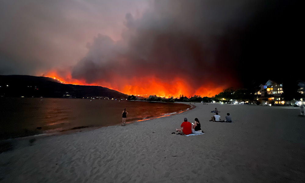 A photo of people on a beach viewing the McDougall Creek wildfire from across Okanagan Lake. 