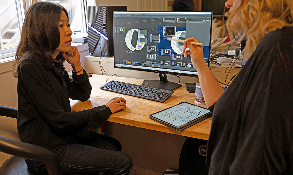 A photo of two women discussing a project in front of a computer monitor