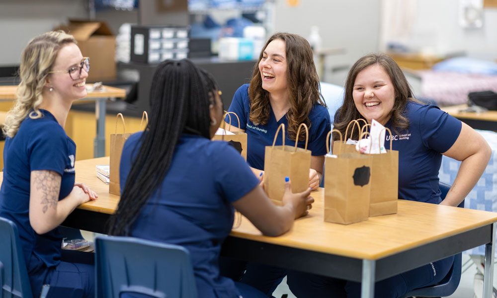 Four nursing students laugh while seated at a table packing foot care goody bags.