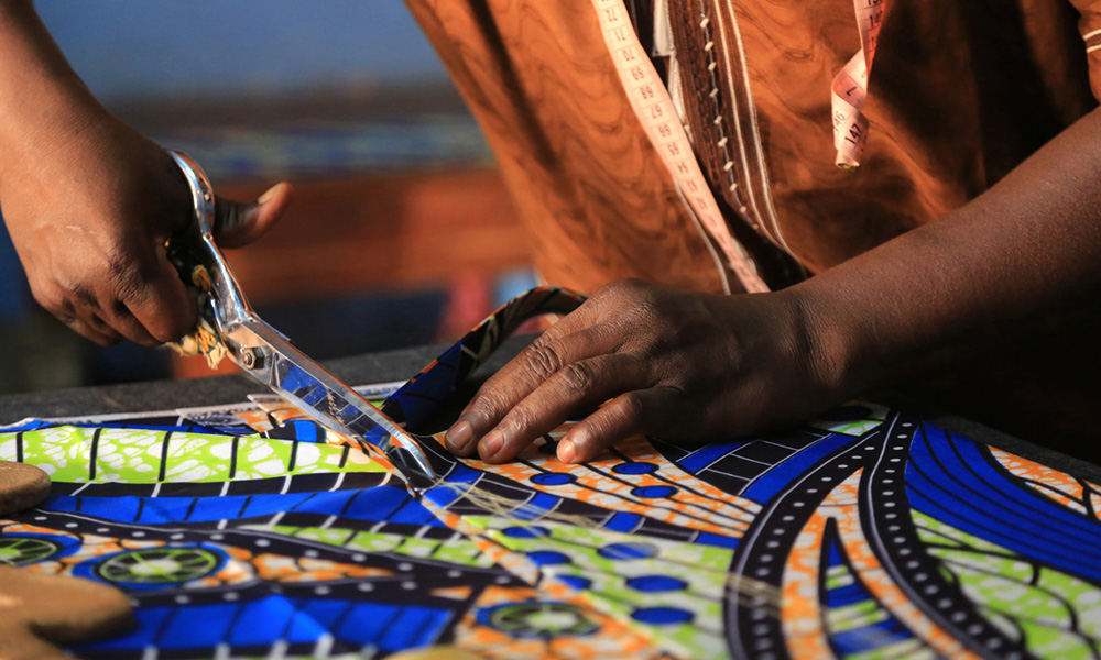 A photo of a woman from Togo cutting fabric