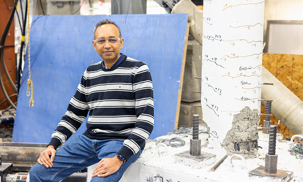 A photo of Dr. Shahria Alam in front of a concrete pillar that has been strength tested and shows lots of wear and tear. 