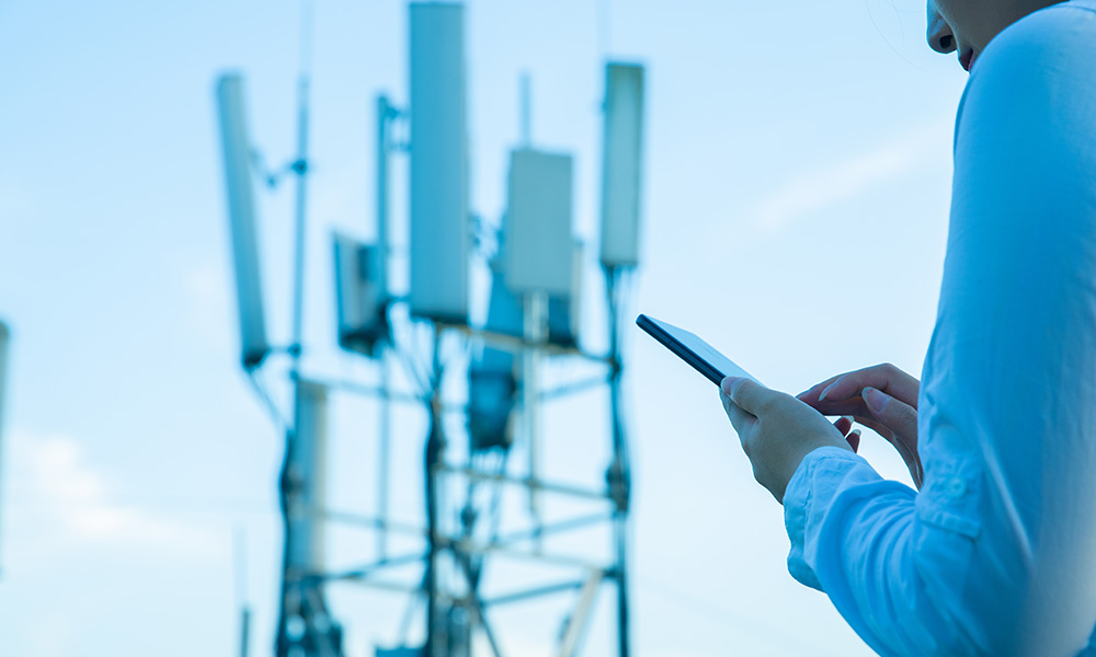 A photo of a person using mobile phone near a 5G communications tower.