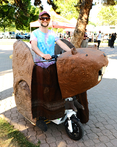 In this community art piece, a man rides a large paper mache beaver mounted on a Lime scooter.