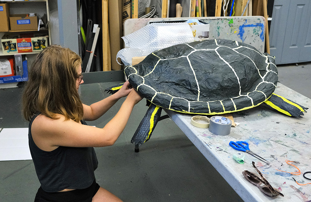 A painted paper mache turtle is receiving some TLC from a workshop participant.