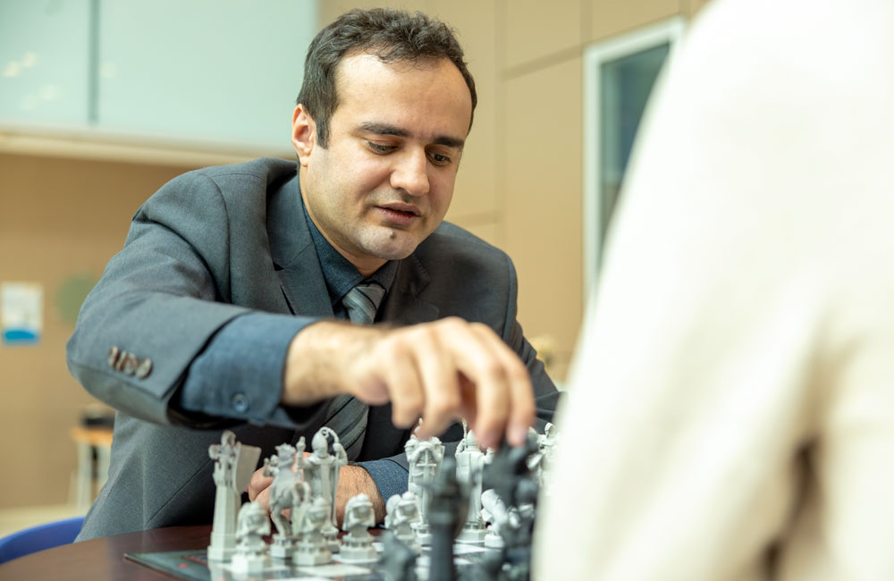 Dr. Amir Ardestani-Jaafari reaches across a chess board moving a piece.