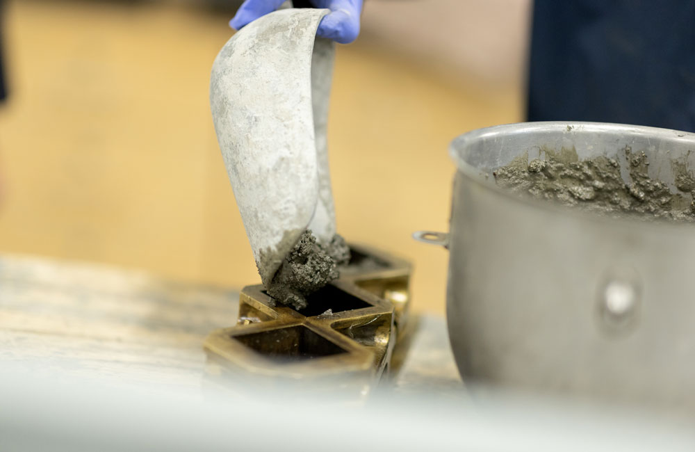 A close up of a trowel spooning cement mixture into a square-shaped mold.