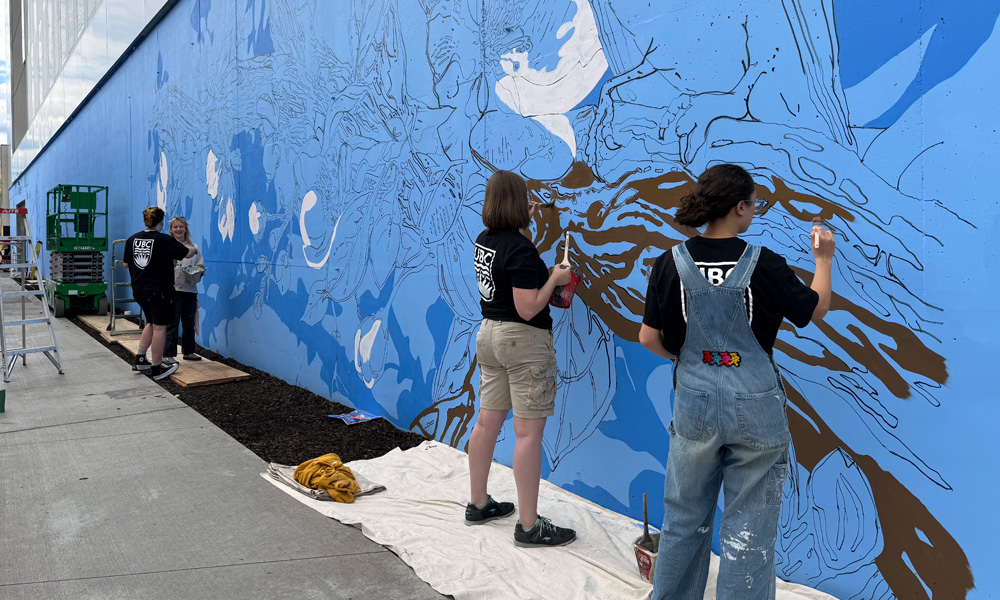 Students work on large blue mural in Landmark District of Kelowna.