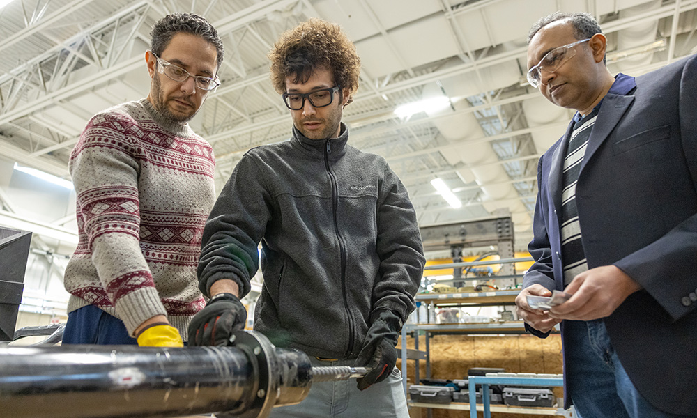 Dr. Shahria Alam stands with two doctoral students as they look at a pipe-shaped item