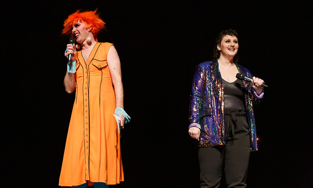 A photo of Pony Cabaret hosts Miss Cookie LaWhore and Erin Scott standing on stage at a previous cabaret.