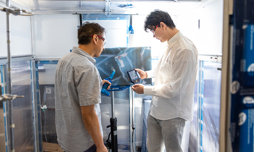 Dr. Sunny Li and student Xudong Wang stand in front of an ART device located in a closed chamber. Dr. Li holds a small carafe that emits fog, while Wang holds a particle counter.