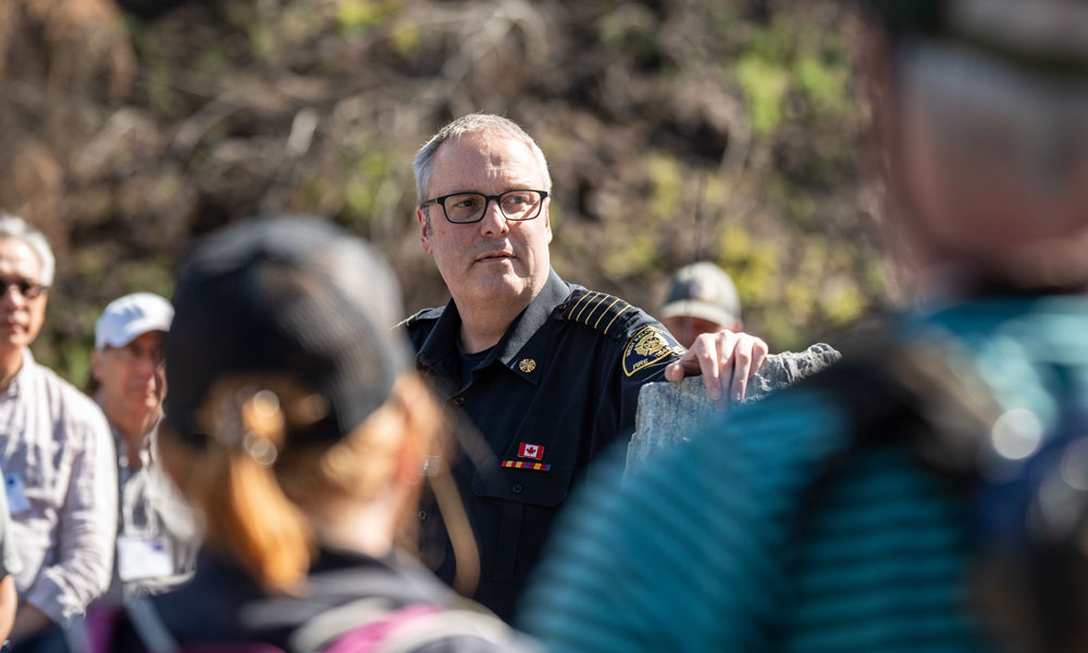 Fire Chief Jason Brolund is seen standing outside surrounded by a crowd of people as he speaks to them about the fire that tore through West Kelowna in 2023